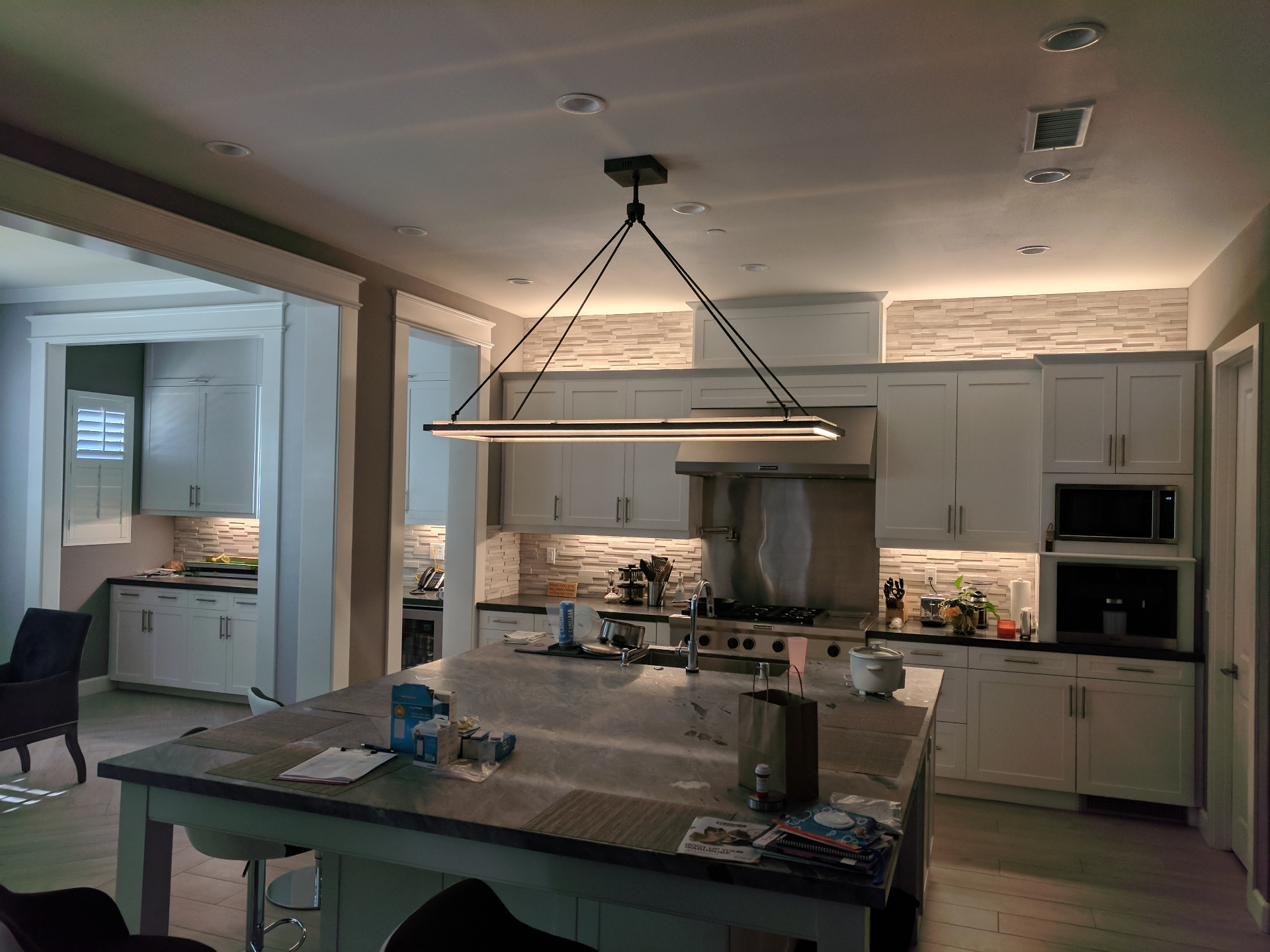 Remodeled kitchen with white shaker cabinets, recessed lighting, and a linear pendant over a large island