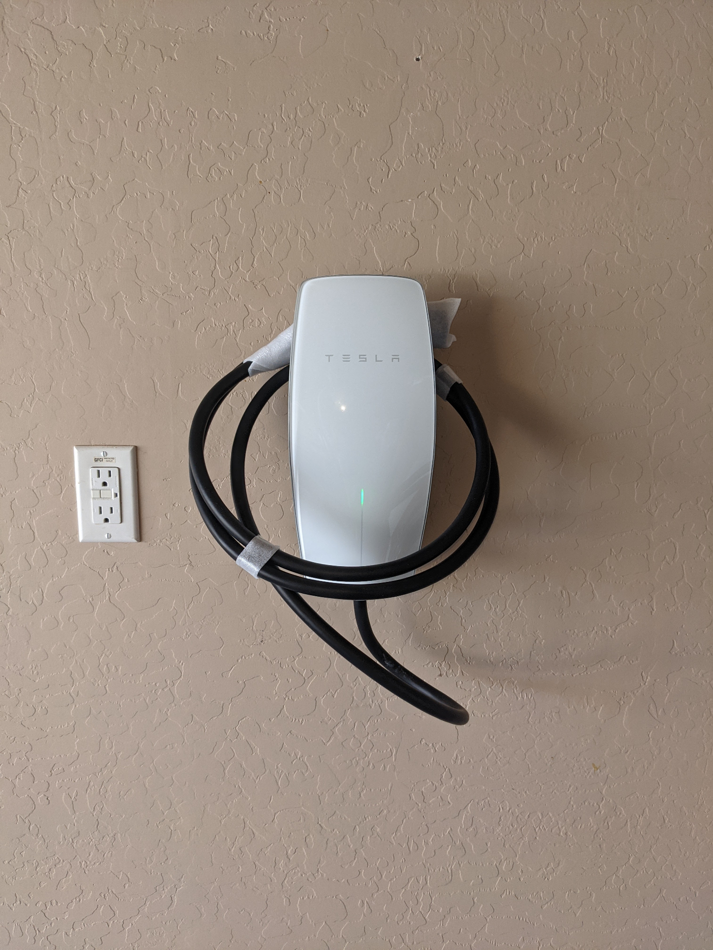 Hardwired Tesla Wall Connector mounted in a residential garage next to a GFCI outlet